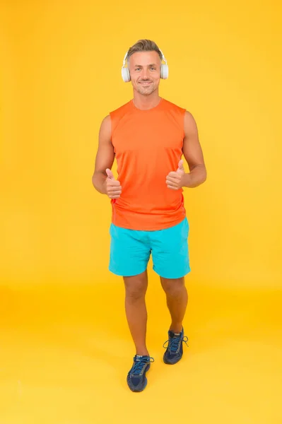Promoting healthy lifestyle. Happy athlete in earphones give thumbs ups yellow background. Approving and promoting. Fitness marketing. Promoting physical activity. Promoting his gym. Health promotion — Stock Photo, Image