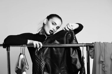 Güzel kız elbise ve askılarda siyah ceketle poz veriyor.