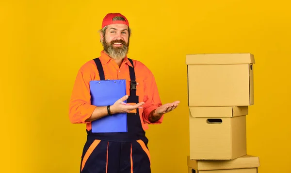 Bartträger in Uniform. Versicherungsvertreter. Bewegender Tag. Sanierungsvorbereitungen. Umzugskartons auspacken. Paketzustellung. Bartträger halten Kartons in der Hand. Umzug in eine neue Wohnung. Post — Stockfoto