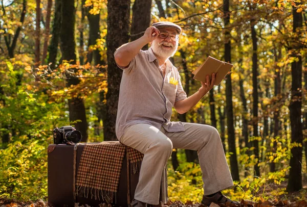 Mature man with white beard in forest. Hobby and leisure. Grandfather with vintage suitcase in nature. United with nature. Weekend in nature. Vacation and relax. Retirement concept. Elderly people