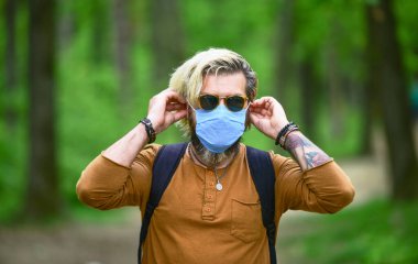 Adam maske takarak hava kirlenmesinden ya da Coronavirus Covid-19 'dan koruyor. Enfeksiyon. Erkek doğa yürüyüşünden hoşlanır. Hava kirliliği yüzünden maske takan bir adam. Yaz gözlüğü tak
