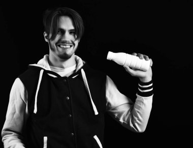 Siyah stüdyo arka planında beyzbol ceketli gülen adam.