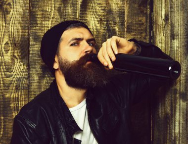 Sakallı vahşi beyaz hippi şişeden içiyor.