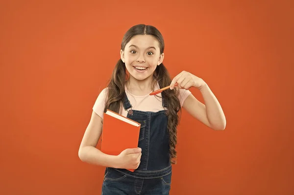 Qué libro tan interesante. lección de literatura. de vuelta a la escuela. niña feliz con cuaderno. poesía y novela. educación moderna. escribiendo notas. Diario de niños. niña de la escuela leer libro sobre fondo naranja — Foto de Stock