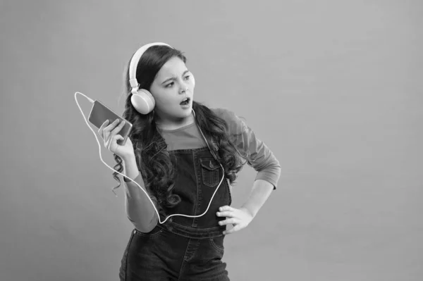 Niña pequeña utilizar reproductor de mp3. estudiar en la vida moderna. colegiala utilizar dispositivo digital. moda casual para niños. cabellos largos escuchar música en los auriculares. niño pequeño hacer lista de juegos en el teléfono inteligente. espacio de copia — Foto de Stock