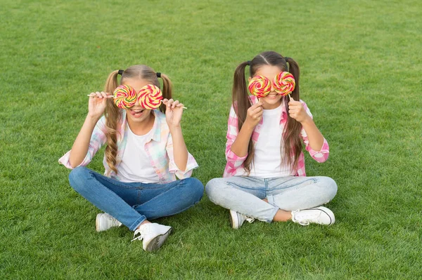 Non seulement doux mais magnifique à regarder. Petites filles au regard doux sur l'herbe verte. Les enfants heureux couvrent les yeux avec des bonbons. Douces friandises. Un magasin de bonbons. Des sucreries. La vie est douce, profitez de tout — Photo