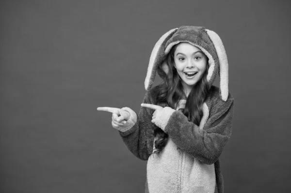 Míralo. Hermosa chica en traje de conejito. Niño en conejo kigurumi. Chica feliz en pijama de conejo. Concepto de estilo de vida. Descansa y relájate. Lindo conejito sobre fondo rojo. Papel de personaje animal bebé — Foto de Stock