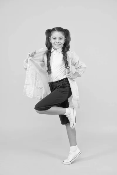 Concepto impermeable. Pequeña colegiala usar ropa resistente al agua para el día de lluvia. Linda colegiala sentirse protegido por el clima de primavera. Adorable niña. Feliz colegiala usar impermeable sobre fondo amarillo —  Fotos de Stock