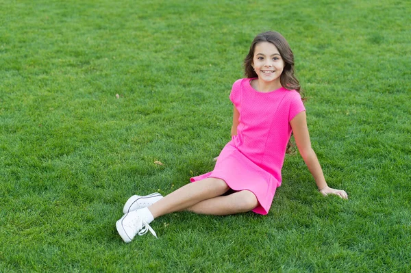 Grön sommar. Ett litet barn sitter på grönt gräs. Liten flicka njuta av sommardagen. Trevlig sommarsemester. Mode sommartrender. Barnkläder — Stockfoto