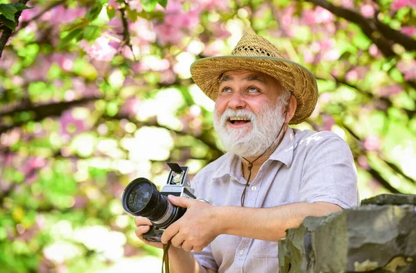 Viagem de aposentadoria. Cursos de fotografia. Viagens e turismo. Capturar a beleza. Avô feliz. Férias. Foto de viagem. Fotógrafo no jardim florescente. Senior man hold câmera profissional — Fotografia de Stock