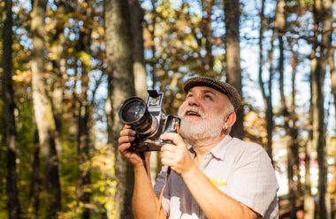 Retro kamera. Anı yakala. Emeklilik ve emeklilik. Eski fotoğraf makineli adam fotoğrafçısının klasik stil fotoğrafı. Sonbahar doğa geçmişi. Gülümse. Kamerayı tutan bir turist. Ormanda güzel bir hafta sonu.