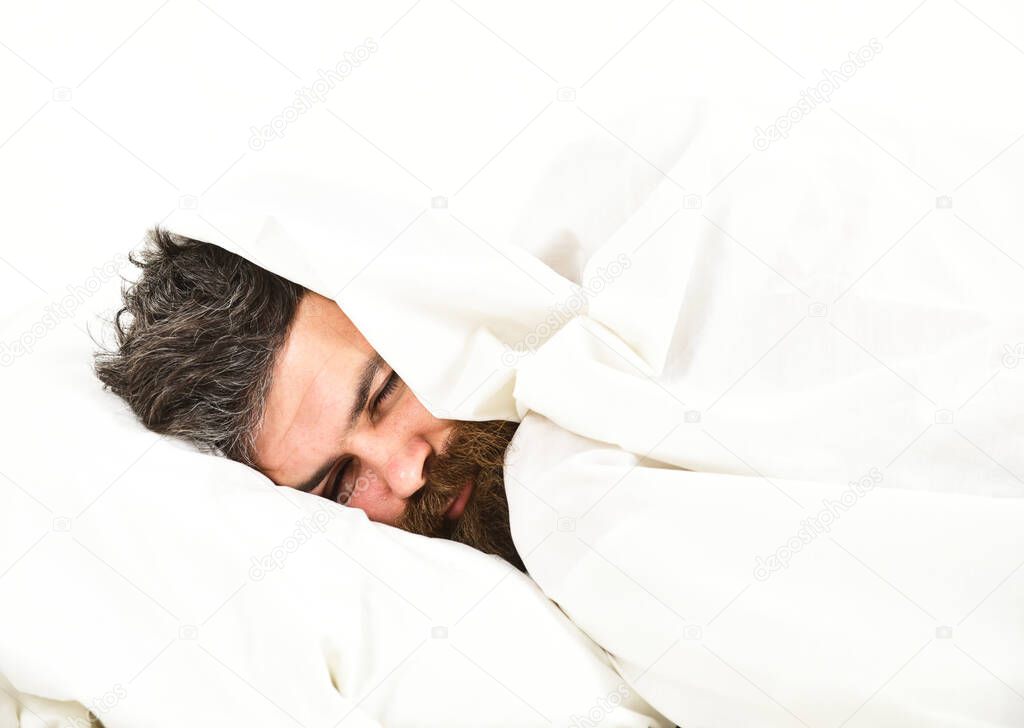 Man with sleepy face lies on pillow under blanket.