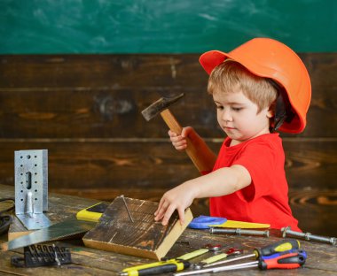 El işi konsepti. Meşgul suratlı çocuk, atölyede çekiç aletleriyle oynuyor. Miğferli şirin çocuk inşaatçı ya da tamirci olarak oynuyor, tamir ediyor ya da el işi yapıyor. Ufaklık elinden her iş gelir.