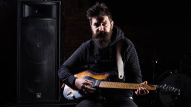 Siyah elbiseli adam gitar tutuyor, hoparlörlerin yanında müzik çalıyor.,