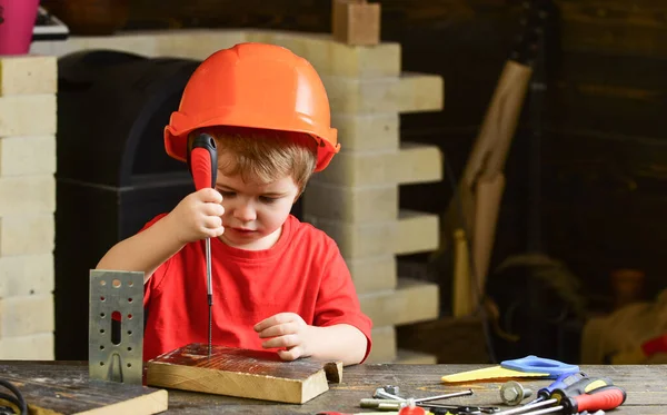 Çocuk inşaatçı ya da tamirci olarak oynuyor, aletlerle çalışıyor. Mimarlık ya da inşaat sektöründe geleceğin hayalini kuran bir çocuk. Turuncu şapkalı ya da kasklı çocuk, çalışma odası arka planında. Çocukluk kavramı.