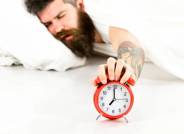 El tipo con la cara somnolienta sostiene el despertador . —  Fotos de Stock