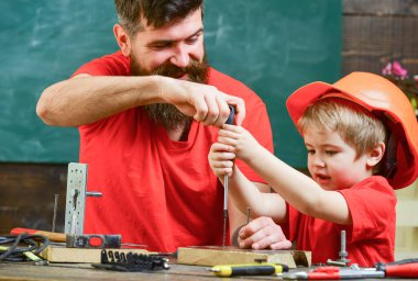 Boy, child busy in protective helmet learning to use screwdriver with dad. Father, parent with beard teaching little son to use tool screwdriver. Teamwork and assistance concept. clipart