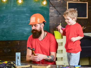 Çocuk neşeli oyunlar ve babayla alet kullanmayı öğreniyor. Babalık kavramı. Baba, koruyucu başlıklı sakallı bir ebeveyn küçük oğluna okulda farklı aletler kullanmayı öğretiyor.