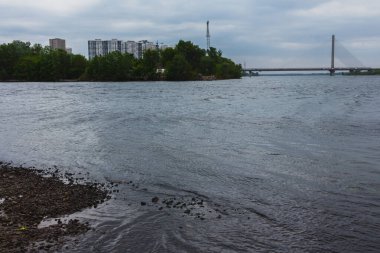 Şehrin peyzaj fotoğrafı. Nehir manzaralı, karşı kıyıda evler ve bir köprü var..