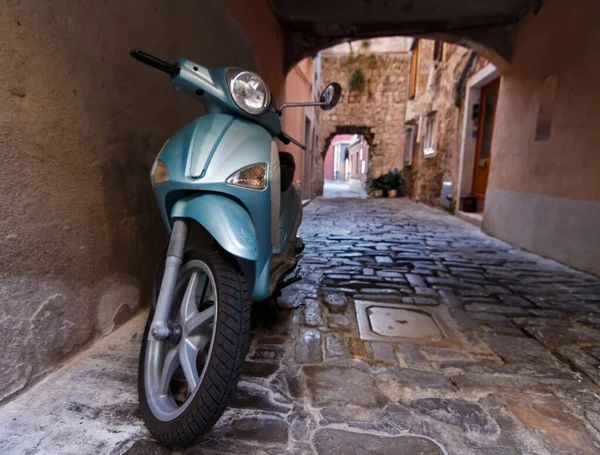 Motor scooter. A motorcycle stands under an arch in Piran.