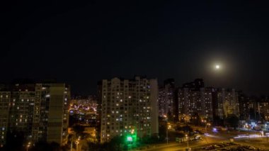 Kavşakta trafik ve gökyüzünde dolunay olan bir gece şehrinin zamanı..
