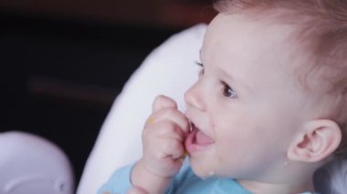 Evde kahvaltıda bir yaşındaki bir çocuğun portresi. Gülümseyen güzel oğlan meyve yiyor..