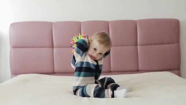 Ritratto di un bambino di un anno che sta giocando con un giocattolo di plastica colorato seduto sul letto. Bambino divertendosi apprendimento precoce. Giocattoli di sviluppo — Video Stock