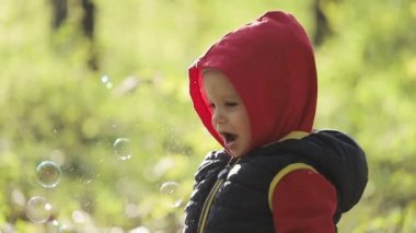 Küçük mutlu çocuk sabun köpüğü yakalıyor. Şirin küçük çocuk oyun oynayarak sabun köpüğü yakalıyor. Parkta sabun köpüğüyle eğlenen mutlu küçük çocuğun portresi..