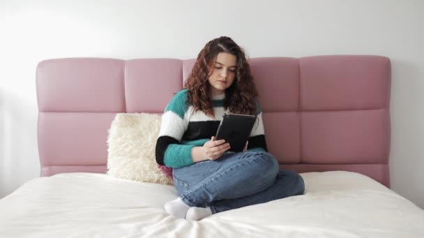 Hermosa mujer usando una tableta en su dormitorio. Mujer joven embarazada hermosa usando tableta digital y sonriendo en la cama. Mujer reloj en tableta ordenador en la cama . — Vídeos de Stock