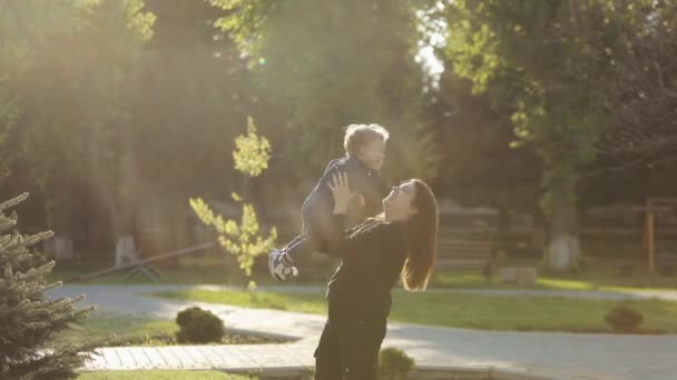 Feliz madre alegre sosteniendo a su pequeño hijo en alto en las manos y riendo en el parque. Exterior . Videoclip