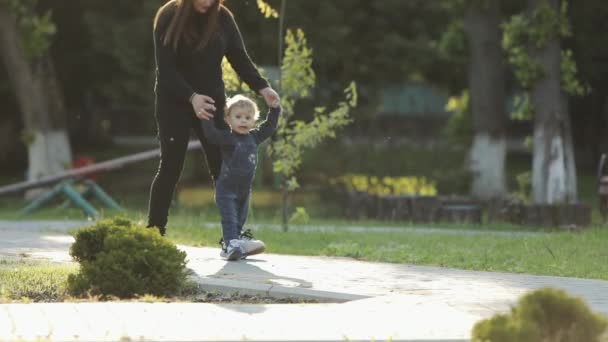 Lindo niño caminando con la madre en el parque, mamá sosteniendo la mano del bebé niño . Video de stock