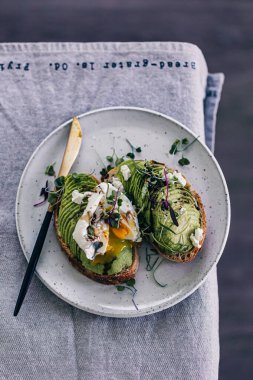 Mikro yeşil ve haşlanmış yumurtalı avokado tostu. Yumurta sarısı tabağa dökülüyor. Minimalist yemek tasarımı. Gri arka plan. Avokado ekmeği dilimleri. Mikro yeşiller. Sağlıklı kahvaltı..