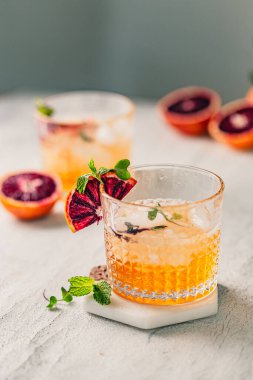 Bardakta yaz kokteyli. Viski bardağı. Citrus soslu buzlu kokteyl. Kan portakalı süslemesi ve taze nane. Beyaz masada serinletici bir yaz kokteyli. Kokteyl gümüş karıştırıcı. Sarı renk.