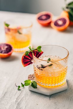 Bardakta yaz kokteyli. Viski bardağı. Citrus soslu buzlu kokteyl. Kan portakalı süslemesi ve taze nane. Beyaz masada serinletici bir yaz kokteyli. Kokteyl gümüş karıştırıcı. Sarı renk.