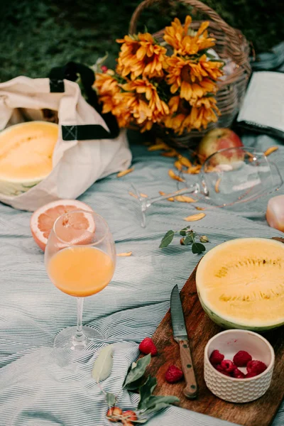 Summer picnic in park. Picnic blanket. Fresh summer fruits melon, grapefruit, orange juice. Summer time picnic fun. Park area, sunflowers in basket. Fresh summer berries. Vacation gathering in park.