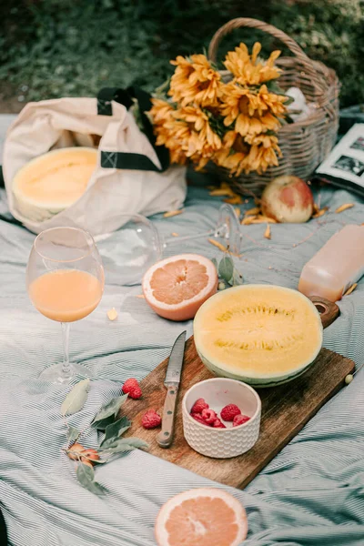 Summer picnic in park. Picnic blanket. Fresh summer fruits melon, grapefruit, orange juice. Summer time picnic fun. Park area, sunflowers in basket. Fresh summer berries. Vacation gathering in park.