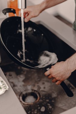 Koca yemekten sonra bulaşıkları yıkar. Kirli bulaşıklar için kazıyıcı. Mutfak lavabosu. Bulaşık deterjanı. Ev ödevi. Evde kal. Karantina sırasında kilitlenme. Yaşam tarzı mutfak. Mutfakta bulaşıkçı var..