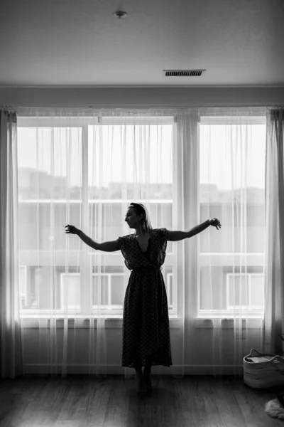 Black and white concept, lady dances in maxi dress in front of the window. Ballerina is dancing. Dance moves. Self isolation stay home coronavirus.Dancer shows neighbors her dancing moves.Grain photos