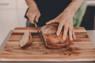 Ev yapımı ekşi ekmek. Buğday çavdar unu. Adam kesme tahtasındaki ekmeği kesiyor. - El yapımı. Gıda trendleri. Tahta kesme tahtası. Erkek eli. Yatay manzara görüntüsü. Evde kal, ekmek pişir..