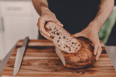 Ev yapımı ekşi ekmek. Buğday çavdar unu. Adam kesme tahtasındaki ekmeği kesiyor. - El yapımı. Gıda trendleri. Tahta kesme tahtası. Erkek eli. Yatay manzara görüntüsü. Evde kal, ekmek pişir..