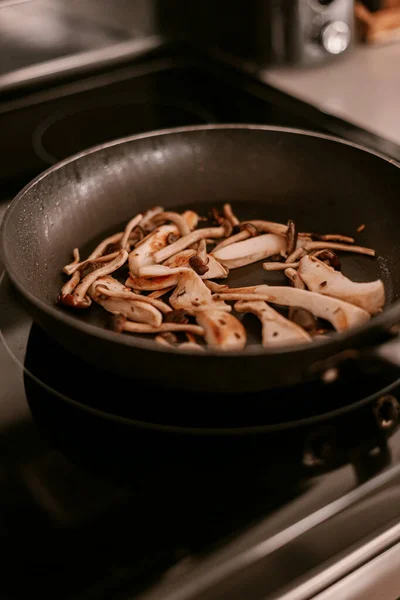 Cooking process on the kitchen. Sauteed mushrooms in frying pan. Cook dinner or lunch. Lifestyle kitchen. White cabinets. Stove top. Pro chef in the kitchen. Cooking tricks. Wild mushrooms.