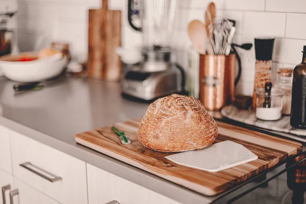 Homemade sourdough bread. Bright white kitchen. Bread on cutting board. Kitchen utensils. Craft authentic bread. Home cooking. Food preparation. Coronavirus covid-19 stay home isolation quarantine.