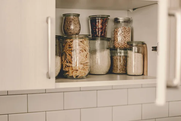 Kitchen storage organization. Zero waste, plastic free. Pasta, grains in glass jars. Organic food. Home cooking. Pantry food cabinet. Nutrition food. Glass containers. Food preparation. Stay home.