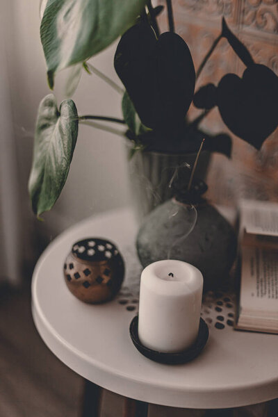Aromatherapy at home. Candle, aroma sticks in grey vase on white side coffee table. Bohemian style. Home plant. Bohemian apartment design. Calmness and relaxation. Sensational time. Meditation at home