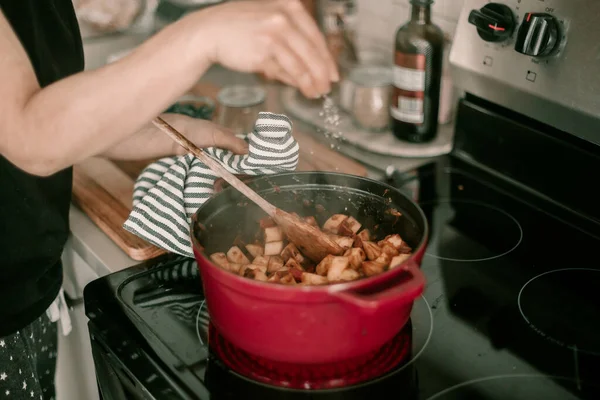 女性は家族のために夕食を作る ストーブの上にオランダのオーブン ライフスタイルキッチン 煮込みジャガイモ 塩で味付け 食事を刺激 熱い食事だ 調理プロセス 夕食の準備 キッチンタオル — ストック写真