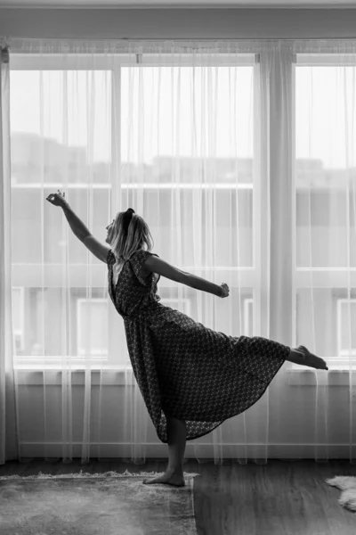 Black and white concept, lady dances in maxi dress in front of the window. Ballerina is dancing. Dance moves. Self isolation stay home coronavirus.Dancer shows neighbors her dancing moves.Grain photos