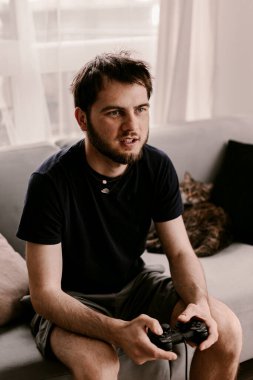 Hippi adam kanepede video oyunu oynuyor. Dinlenme zamanı. Eğlenceli bir hafta sonu. Bir video oyununa odaklanmış. Oyunu kazanmak, kumar oynamak. Çoklu oyuncu oyunu. Çevrimiçi oyun. Yayınlanan video oyunu. Futbol, yarış