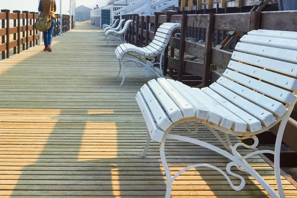 Row of white benches on a wooden boardwalk. Walking woman with a travel bag. End of beach vacation — Stock Photo, Image