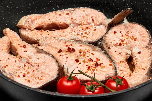 Salmon steaks in a pan with spices. Red fish on a dark background with tomatoes on a branch