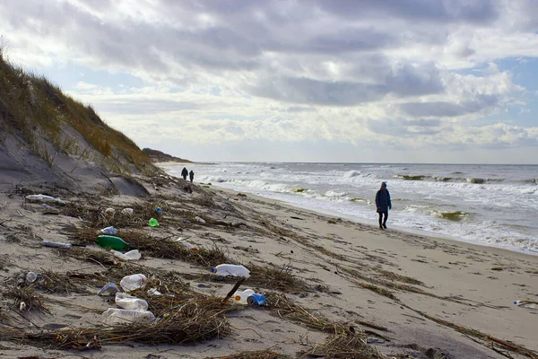 Plajda çöp ve plastik şişeler. Fırtınanın attığı çöpler. Yürüyen insanlar. Kışın Baltık Denizi
